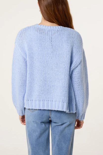 A person with long brown hair is wearing a light blue knitted cardigan and light blue jeans, seen from behind against a plain background.