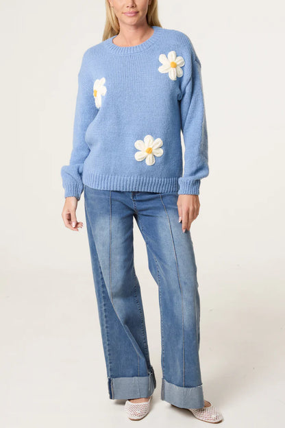 A person is wearing a Flocking Daisy Knitted Jumper crafted from sustainable materials, teamed with wide-leg blue jeans and white trainers, standing against a plain background.