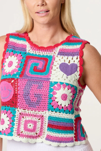 A woman wears a colourful Retro Patchwork Crochet Vest, adorned with hearts, swirls, and flowers in pink, purple, teal, and white—a vibrant garment brimming with 1970s-inspired style.