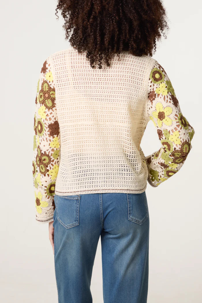 A person dressed in blue jeans and a lightweight crochet jumper with sleeves featuring a floral pattern, seen from behind.