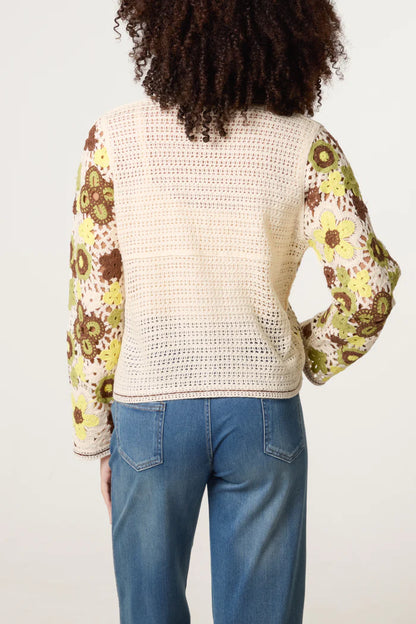 A person dressed in blue jeans and a lightweight crochet jumper with sleeves featuring a floral pattern, seen from behind.