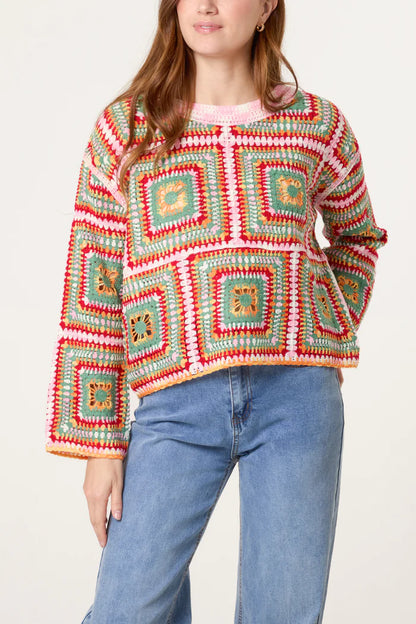 A woman wears a patchwork crochet jumper featuring colourful square patterns in red, green, yellow and white, teamed with blue jeans.
