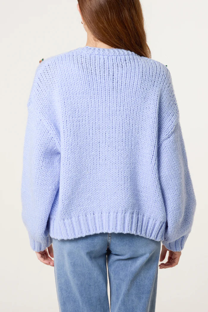 Person wearing an oversized knitted, light blue jumper and blue jeans, seen from behind against a plain light background.