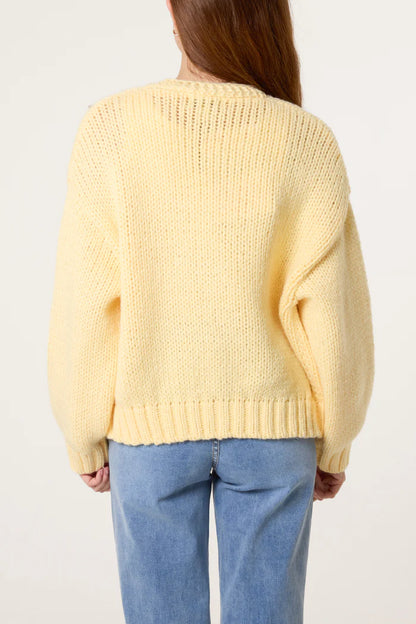 Individual wearing a loose, pale yellow chunky knitted cardigan and light blue jeans, viewed from behind against a plain background.