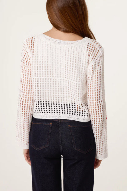 A person with long brown hair is seen from behind, wearing a white, handmade crochet jumper and high-waisted dark blue jeans.