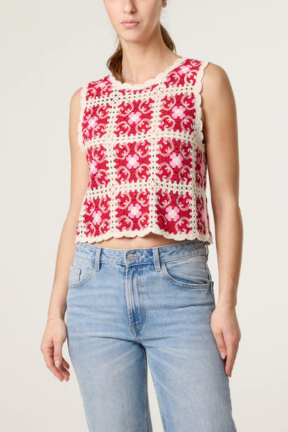 A woman in a bohemian crochet top with a scalloped hem, featuring red and white colours, effortlessly paired with light blue jeans.