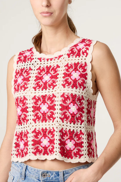 A woman wears a bohemian crochet top—a sleeveless red and cream floral design with scalloped edges—stylishly paired with light blue jeans.