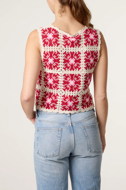 A woman dressed in light blue jeans and a bohemian red and white crochet waistcoat, seen from behind against a plain backdrop.