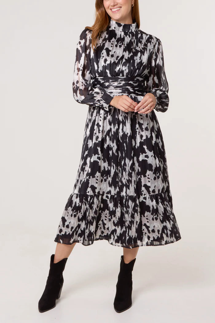 A woman in a long-sleeved, black and white abstract print dress featuring a fitted waist and tiered skirt, teamed with black ankle boots.