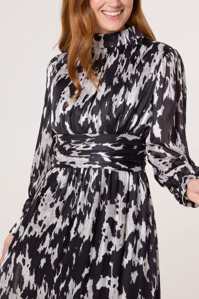 A woman wears a long-sleeved, high-neck abstract print dress in black and white, featuring a wide waistband for a belted dress silhouette.