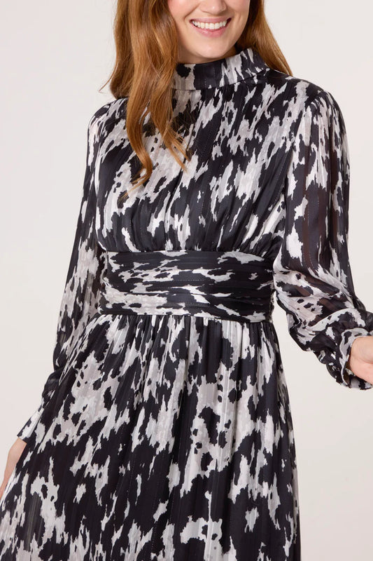 A woman wears a long-sleeved, high-neck abstract print dress in black and white, featuring a wide waistband for a belted dress silhouette.