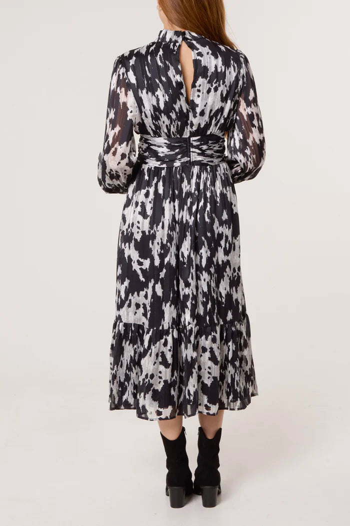 A woman is seen from behind wearing a black and white abstract print midi dress with long sleeves and black heeled boots.
