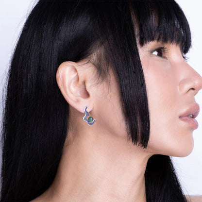 Individual with long black hair wearing a silver, snake-shaped aventurine earring featuring a green gemstone, shown in profile against a plain backdrop.