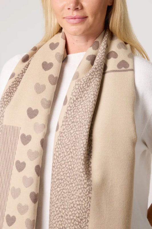 A woman wearing a vegan-friendly, heart-print scarf featuring various brown hearts over a white jumper.
