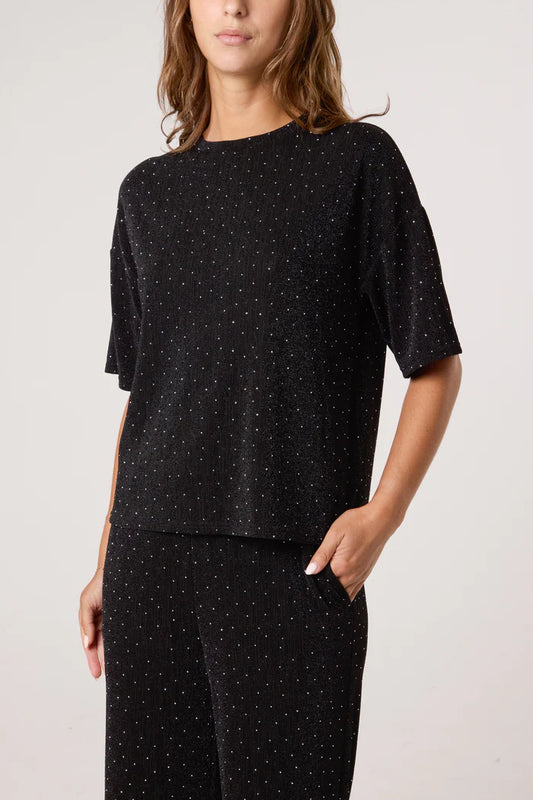 A person in a black trouser suit with a subtle dotted pattern stands with one hand in their pocket—a stylish, festive outfit suitable for any occasion.