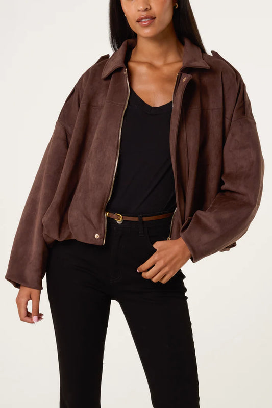 A woman in a chocolate suedette jacket over a black top and black trousers, standing against a plain background.
