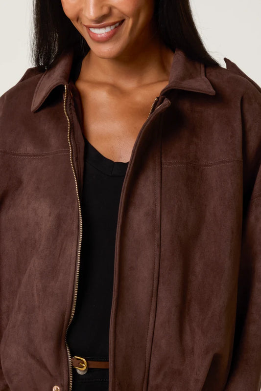 A woman smiles, dressed in a chocolate suedette jacket over a black top, with just the lower half of her face visible.