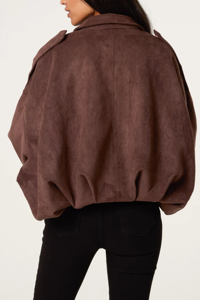 A woman seen from behind wearing a chocolate suedette jacket with broad shoulders, paired with black trousers.