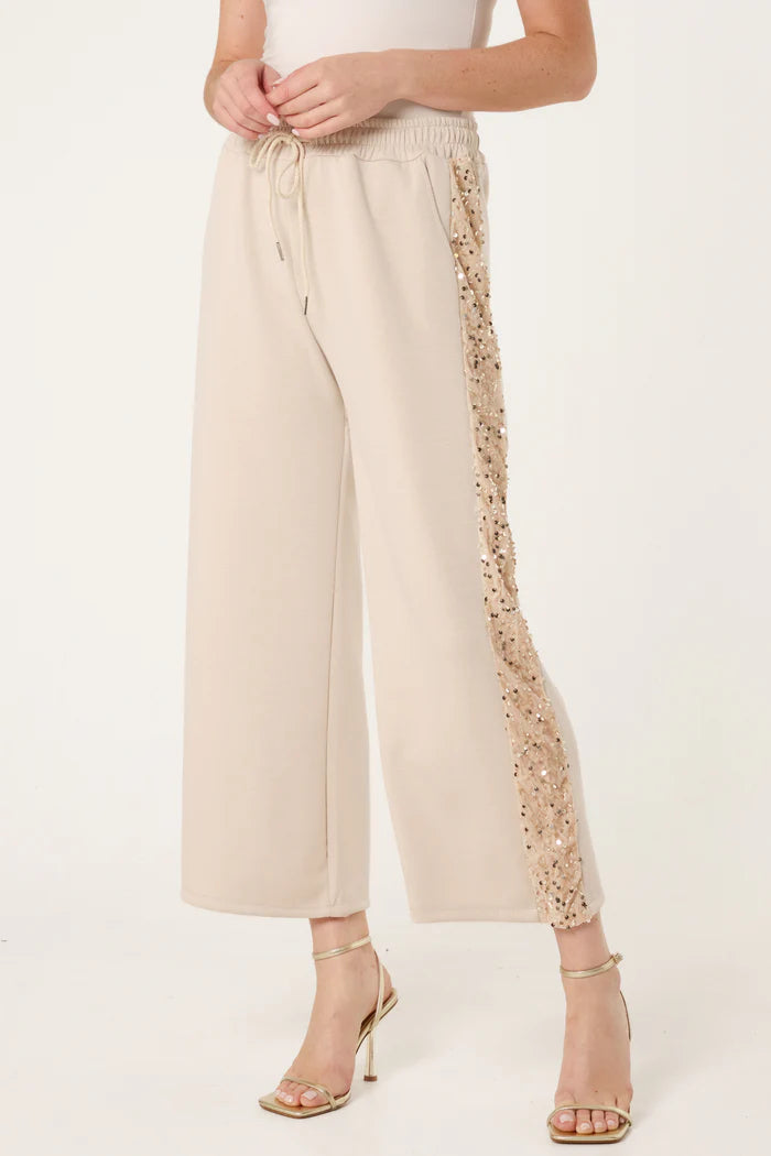 A person wearing cream-coloured wide-leg trousers with sequin detailing from the Italian collection, paired with a white top and heeled sandals for a chic athleisure touch.