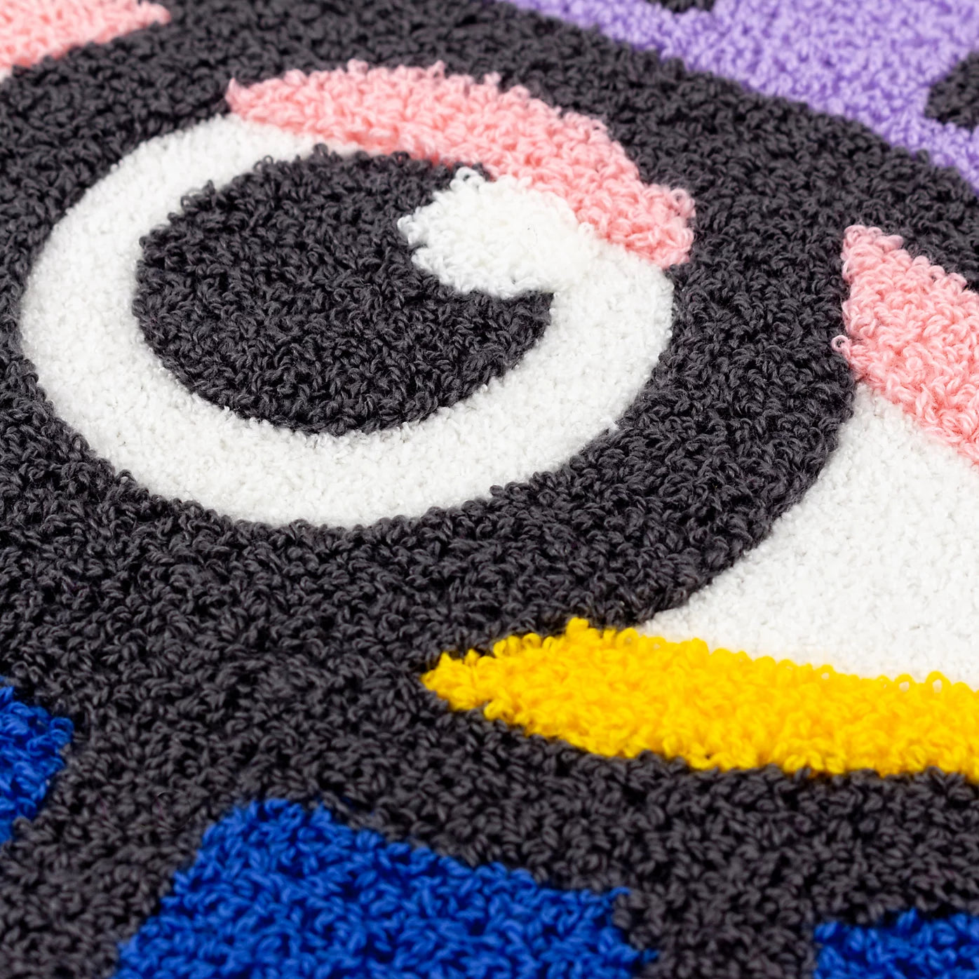 Close-up of a textured, colourful, tufted rug featuring a cartoonish eye design in black, white, pink, yellow, blue and purple—ideal to pair with a cosy purple-blue cushion.