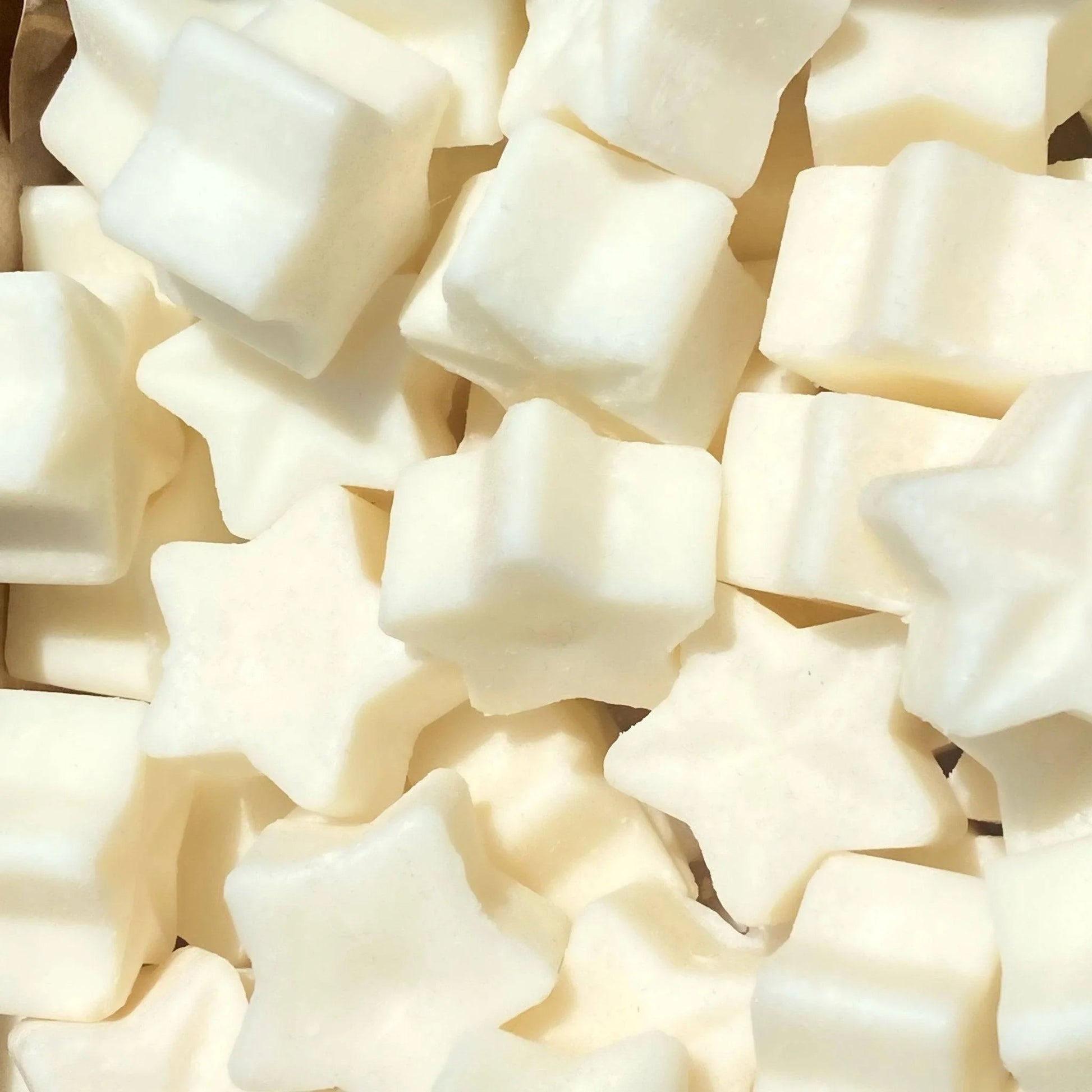 A collection of star-shaped and square-shaped white marshmallows, reminiscent of vegan wax melts, viewed from above and closely packed together.