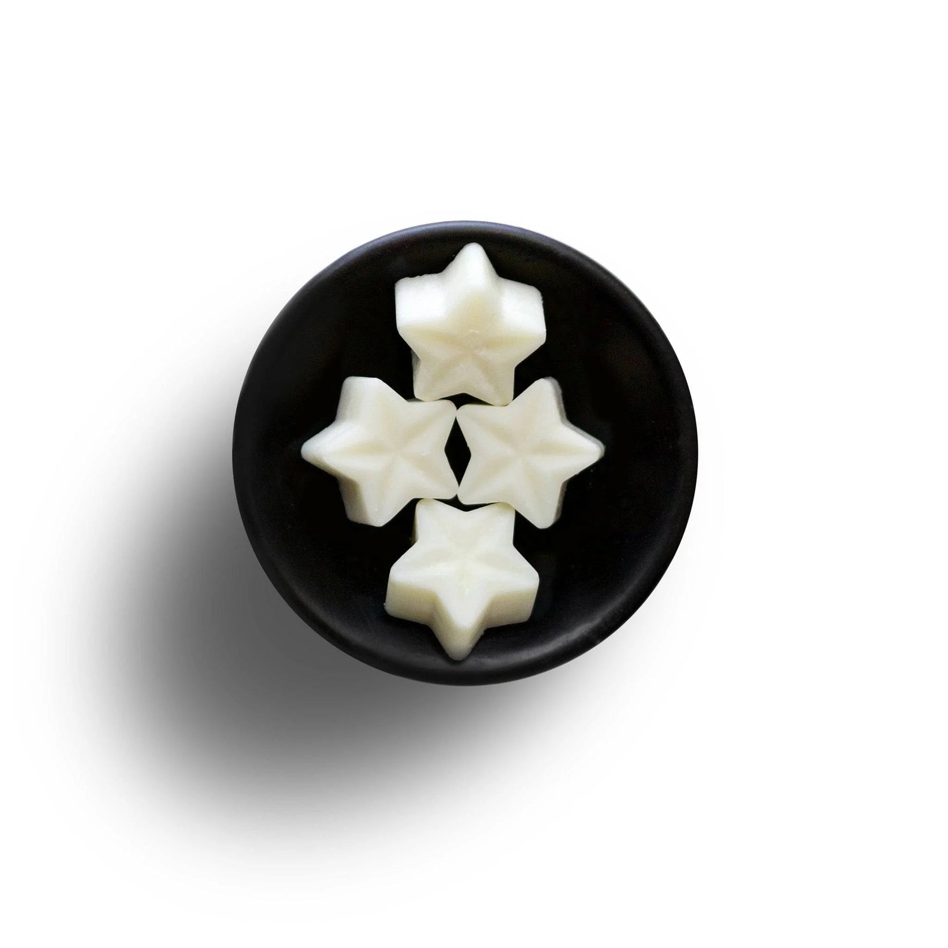 Four star-shaped white sweets in a black bowl on a white background, elegantly reminiscent of vegan wax melts.