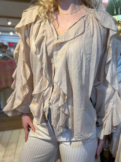 Person wearing a loose, light beige Ruffle Front Shirt featuring ruffle details and long sleeves, paired with light-coloured, vertically striped trousers—an effortless display of feminine elegance.
