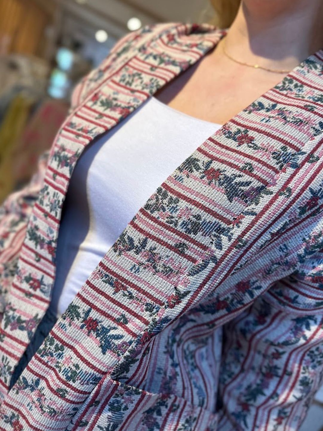Close-up of a person dressed in a white top and an eye-catching jacket with red, green, and blue floral and stripe patterns. The person’s face is partially out of the frame.