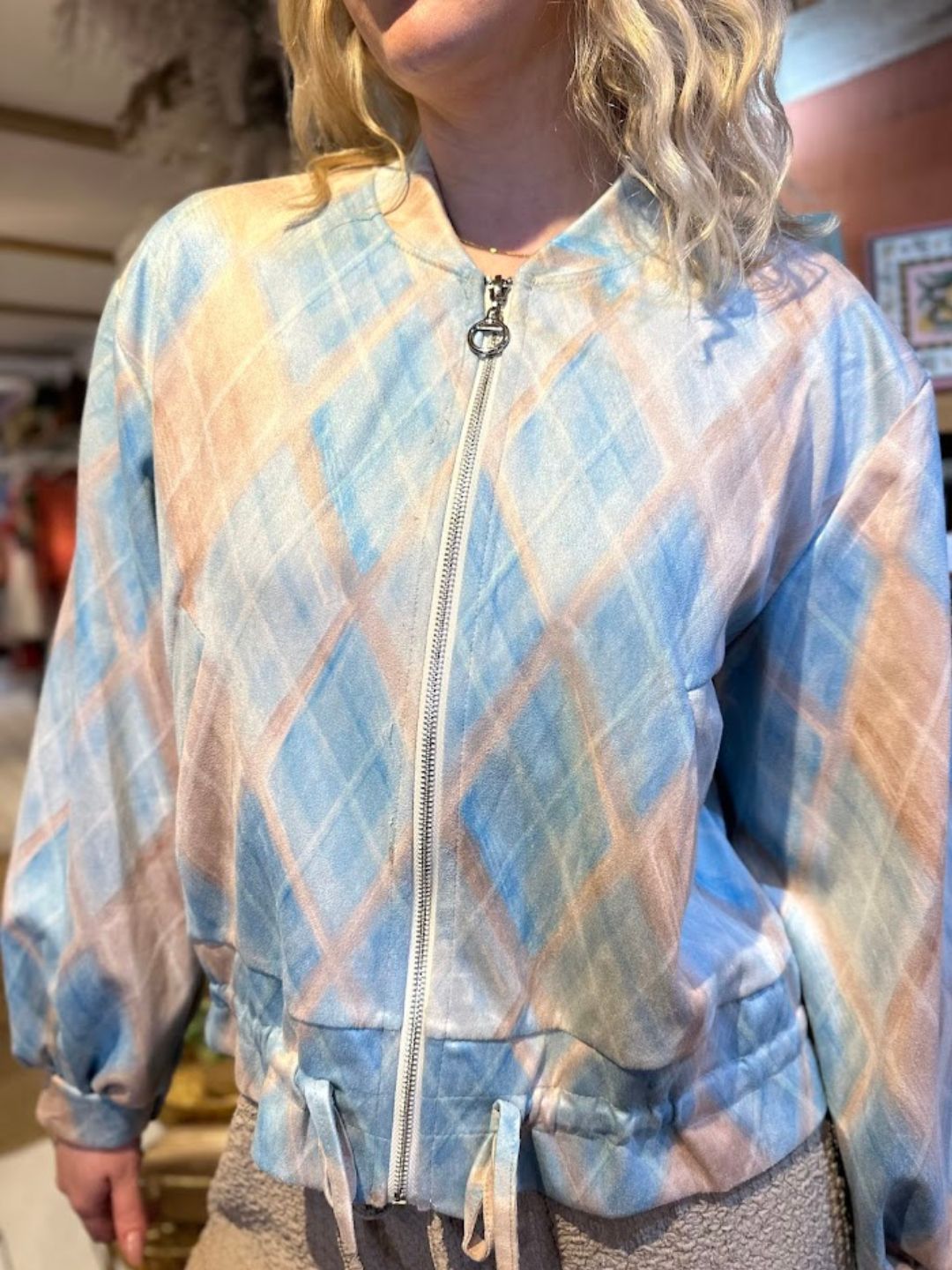 A person wearing a pastel-coloured, diamond-patterned colour-block jacket with a zip-up front and drawstring waist.
