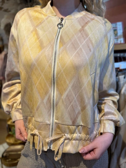A person wearing a light yellow and beige checked bomber jacket with a zip-up front and drawstring hem, standing indoors with hands in their pockets.