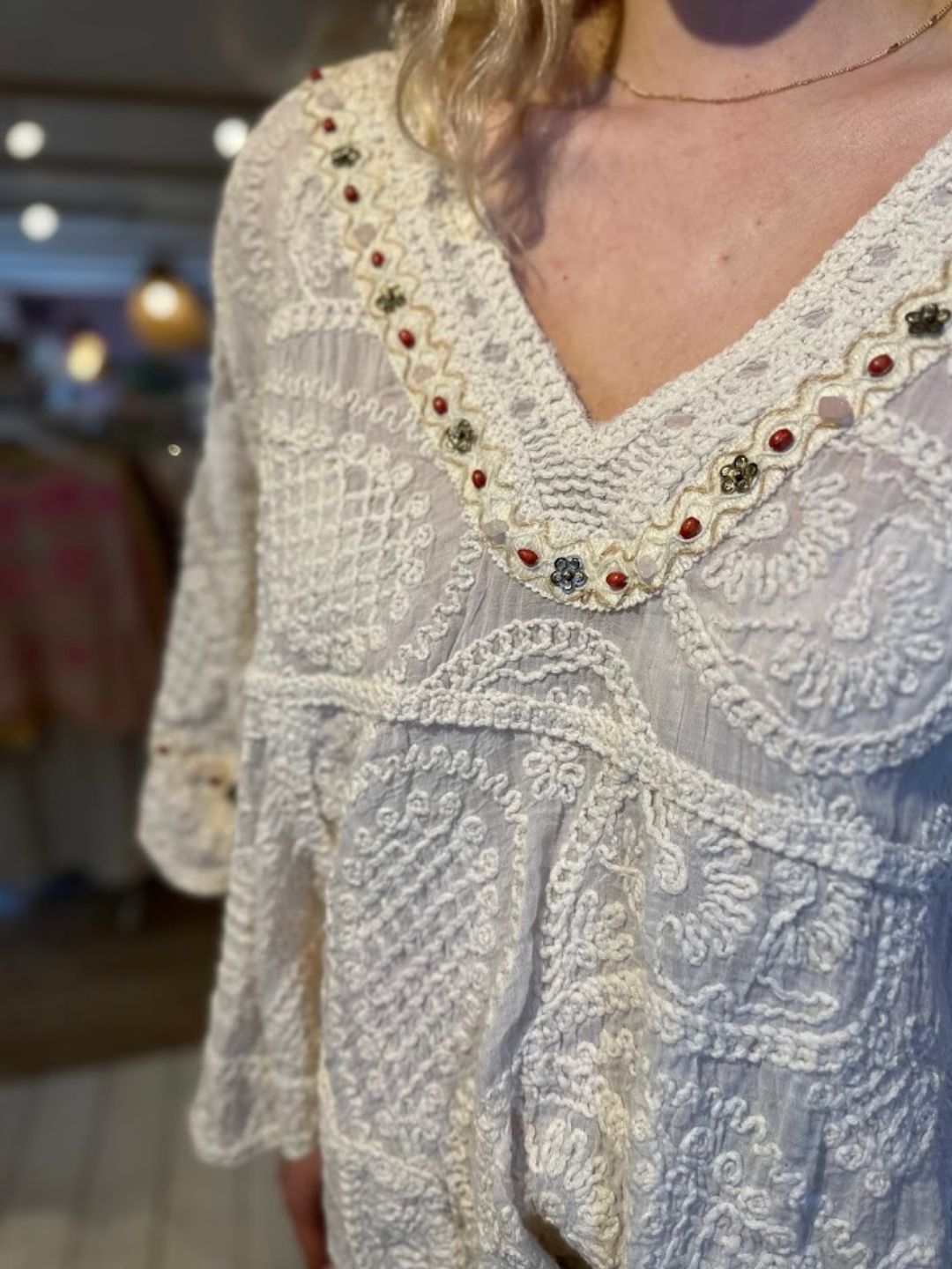 A close-up of a person wearing a white, vintage-inspired top with embroidered floral details along the neckline and sleeves. The background is gently blurred.