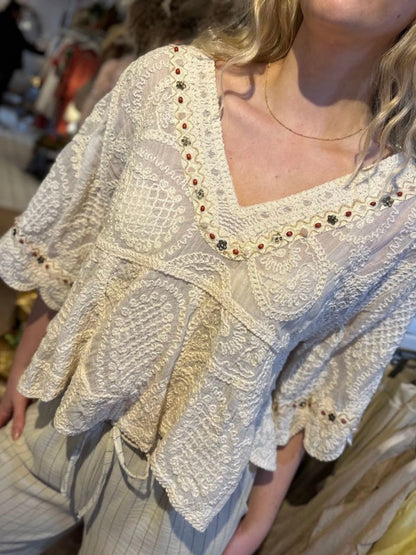 A person wearing a cream-coloured, bohemian blouse with a v-neckline and wide sleeves, paired with light-coloured, pinstriped trousers.
