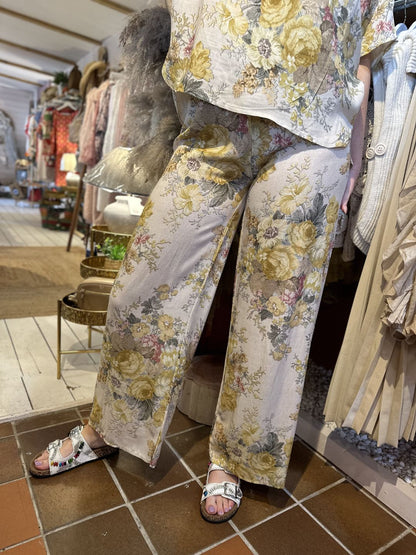 Person wearing a floral co-ord set with wide-leg trousers stands in a boutique, with displays of clothing and accessories visible in the background.
