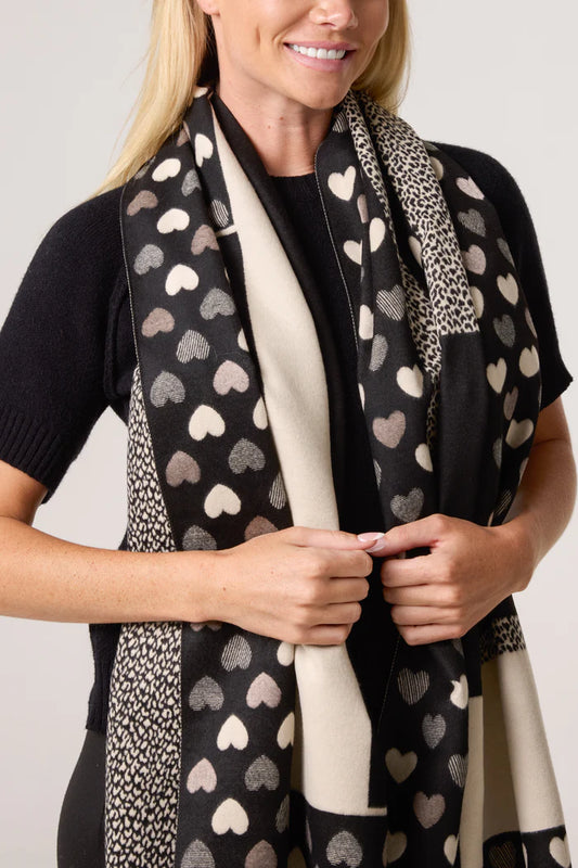 A woman wearing a black short-sleeved top and a reversible vegan heart print scarf decorated with cream and black animal and heart patterns.