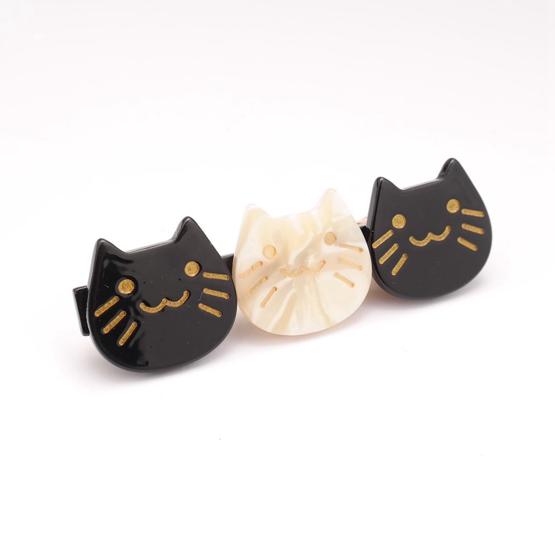 Three cat-shaped hair clips crafted from acetate, featuring smiling cat faces in a black mix and white design, arranged side by side on a white background.
