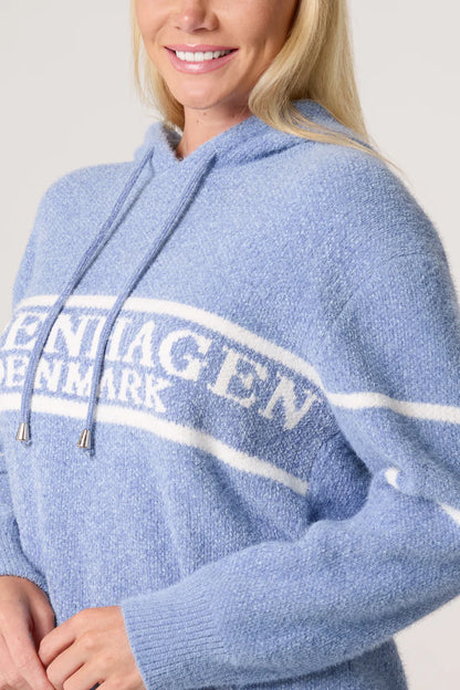 A person wearing a cosy baby blue hoodie with white stripes and the words COPENHAGEN DENMARK printed on the front.