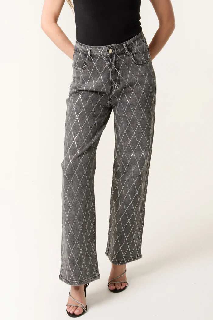 A person is wearing high-waisted, wide-leg diamond-embellished jeans with a white pattern, a black sleeveless top, and black heeled sandals.