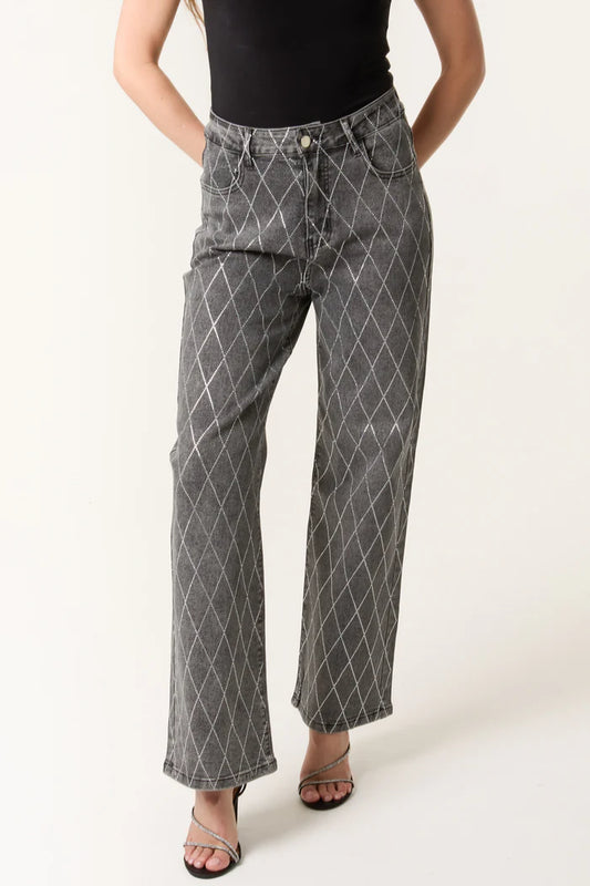 A person is wearing high-waisted, wide-leg diamond-embellished jeans with a white pattern, a black sleeveless top, and black heeled sandals.