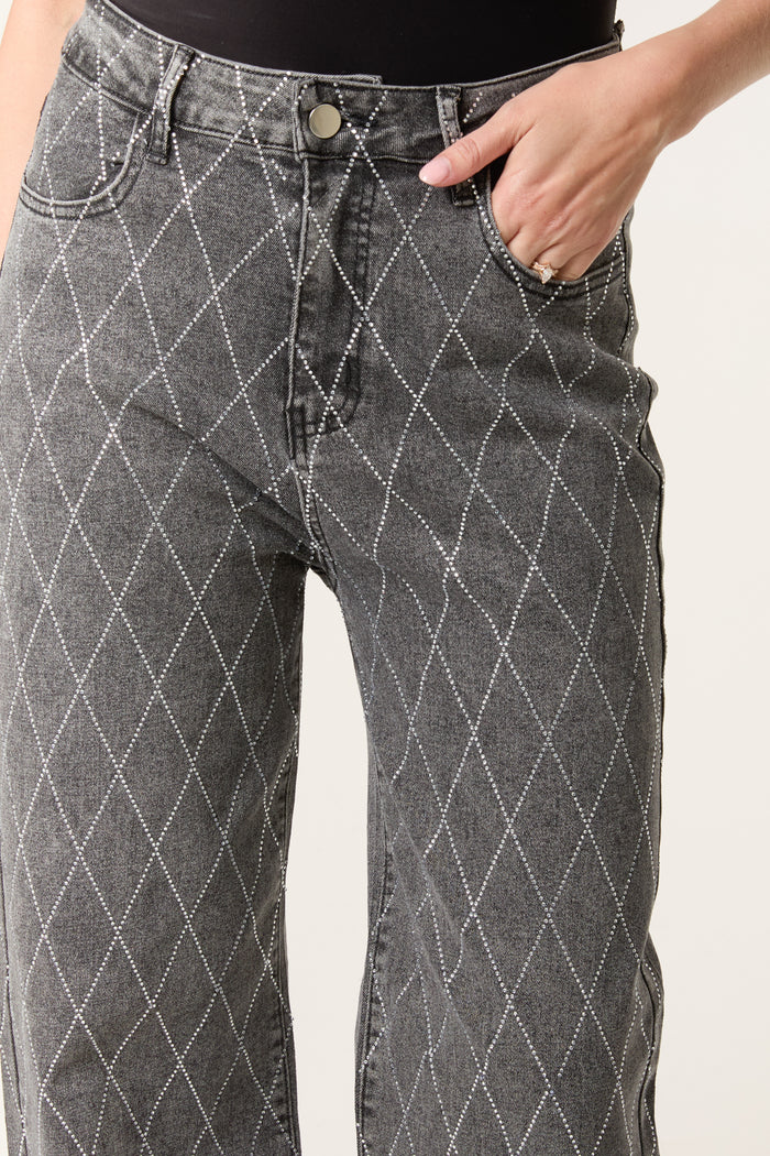 Close-up of a person wearing high-waisted, diamond-embellished grey jeans with a white pattern, one hand in the pocket and the other near the waistband.