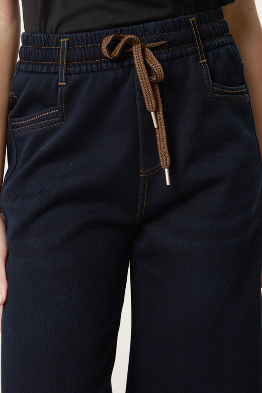 Close-up of a person wearing dark blue relaxed-fit jeans with contrast stitching and a black top, highlighting the elasticated waistband and front pockets.