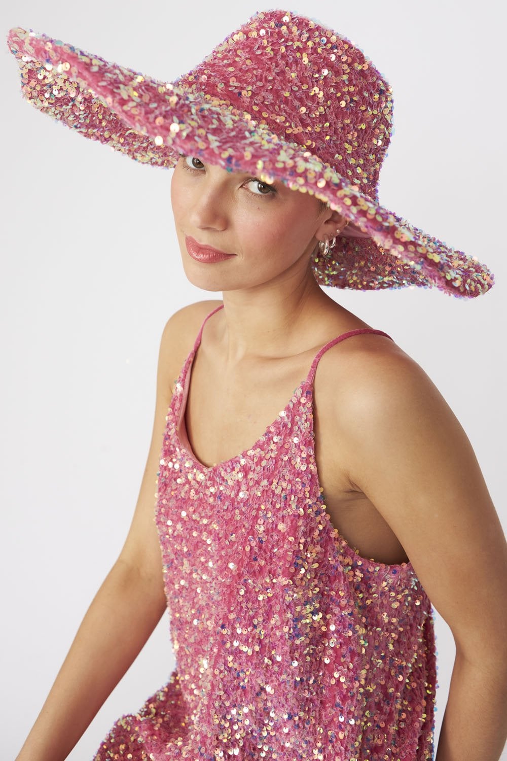 A person wearing a pink sequin flapper hat and a matching pink sequin dress poses against a plain white background, evoking vintage glamour.