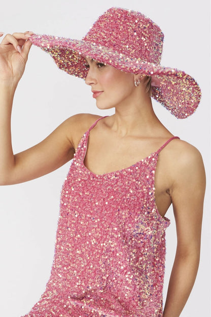 A person in a pink sequin dress and matching handmade flapper hat holds the brim with one hand, posing elegantly against a plain light-coloured background.