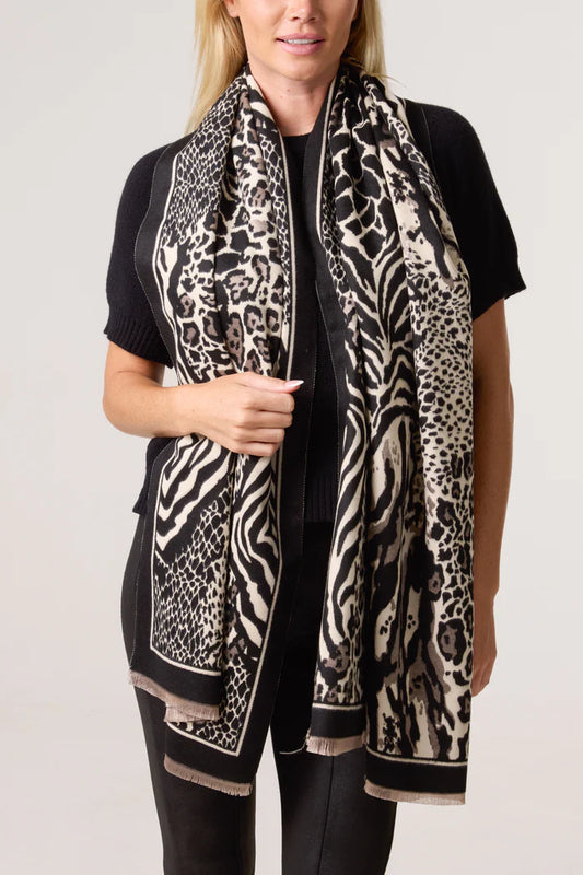 A person dressed in black with a long, vegan-friendly animal print scarf draped about their neck—a striking fashion accessory.
