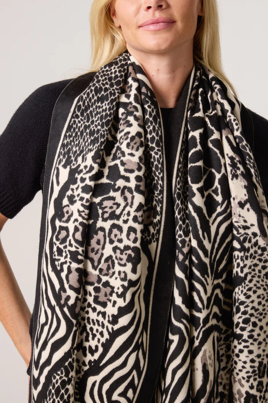A woman in a black top and a large vegan-friendly animal print scarf stands before a plain background, highlighting this striking fashion accessory.