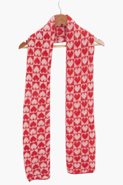 A Red Heart Vegan Scarf with a red and white repeating heart pattern hangs on a wooden hanger against a white background—ideal as your cosy, cruelty-free scarf for winter.