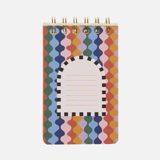 A small spiral flip notebook with a colourful wavy pattern and a central white label bordered in black, featuring lines for writing.