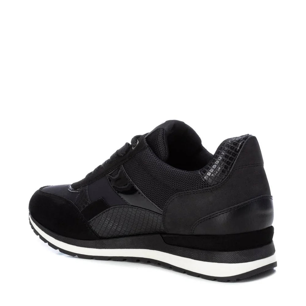 A black women’s trainer made from PETA-certified vegan materials, featuring a mixed-texture design, laces, a removable insole, and a sole with white stripes, viewed from a back-side angle.