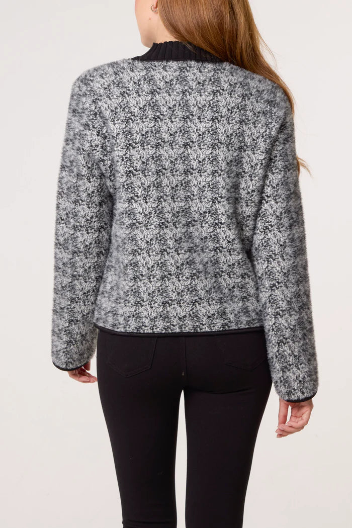 A person is seen from behind wearing a black and grey textured cardigan with long sleeves and black trousers.