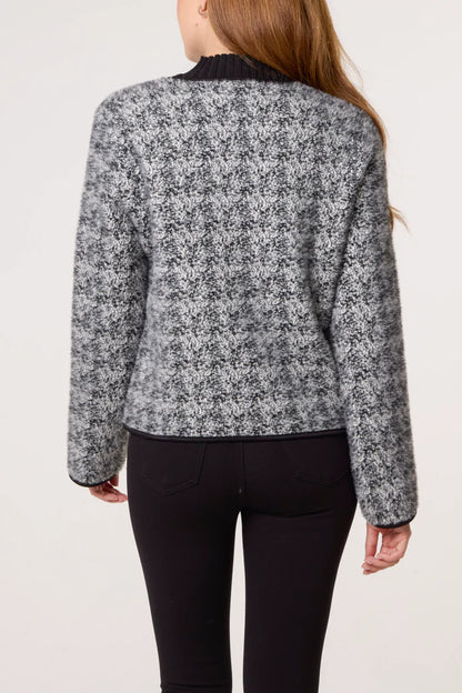 A person is seen from behind wearing a black and grey textured cardigan with long sleeves and black trousers.