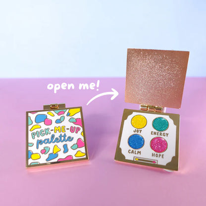 Two colourful square compacts are shown—one closed, labelled Pick-Me-Up Palette enamel pin, and one open, displaying four glittery shades named Joy, Energy, Calm, and Hope; a perfect self-care gift.